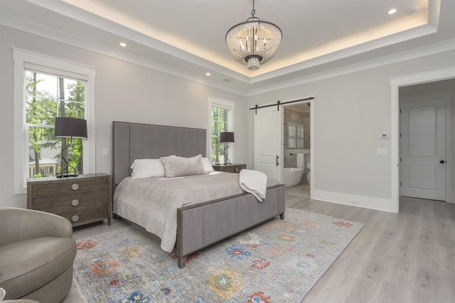 bedroom with ensuite bathroom, an inviting chandelier, light hardwood / wood-style flooring, a tray ceiling, and a barn door