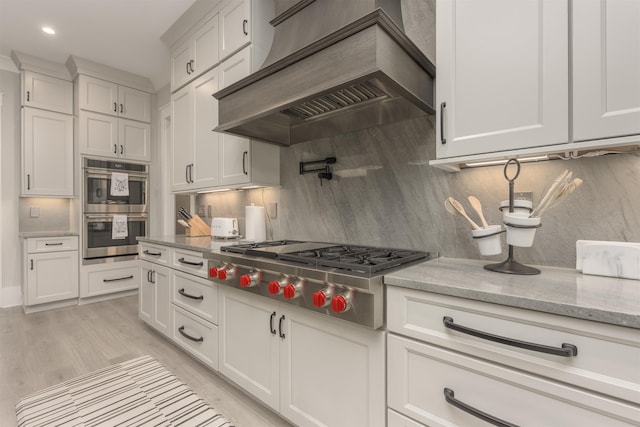 kitchen featuring white cabinetry, appliances with stainless steel finishes, custom range hood, and light stone counters