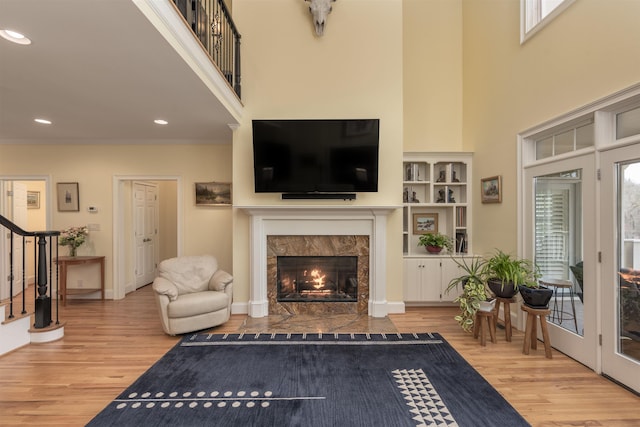 living room featuring ornamental molding, wood-type flooring, a high end fireplace, and a towering ceiling