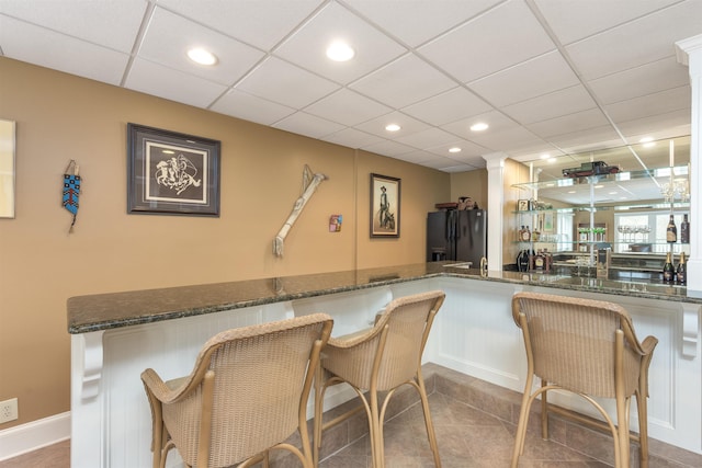 kitchen with a kitchen breakfast bar, dark stone countertops, white cabinets, and black fridge with ice dispenser