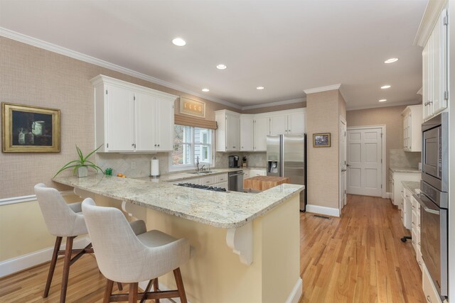 kitchen featuring stainless steel appliances, white cabinetry, light stone countertops, and kitchen peninsula