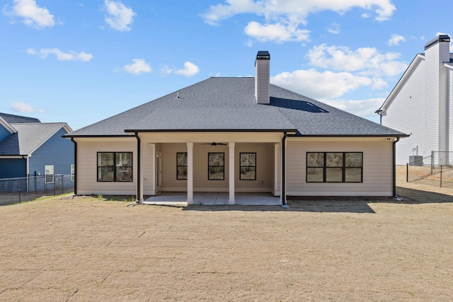 rear view of house with a shingled roof, ceiling fan, fence, a chimney, and a patio