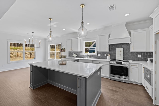 kitchen featuring visible vents, a kitchen island, stainless steel appliances, custom range hood, and crown molding