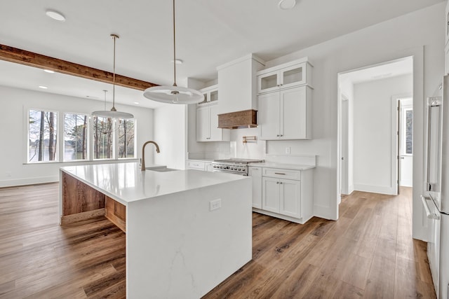 kitchen featuring sink, wood-type flooring, an island with sink, white cabinets, and decorative light fixtures