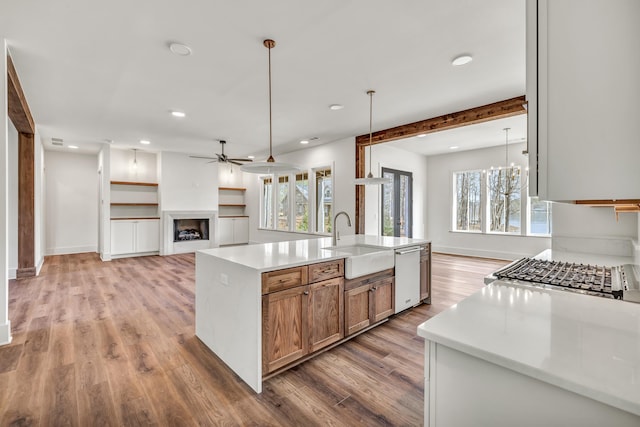 kitchen featuring decorative light fixtures, sink, a kitchen island with sink, stainless steel dishwasher, and light hardwood / wood-style flooring