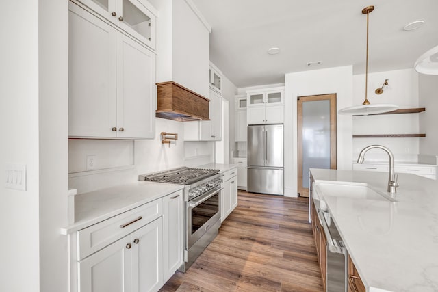 kitchen with sink, white cabinetry, hanging light fixtures, appliances with stainless steel finishes, and hardwood / wood-style flooring