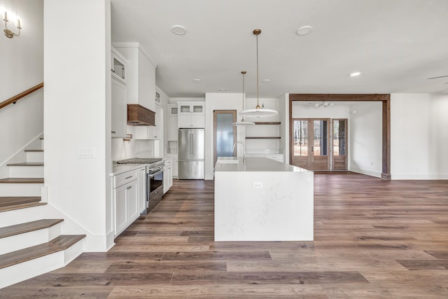 kitchen featuring appliances with stainless steel finishes, decorative light fixtures, an island with sink, white cabinets, and dark hardwood / wood-style flooring