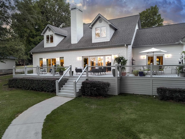 back house at dusk featuring a yard and a deck