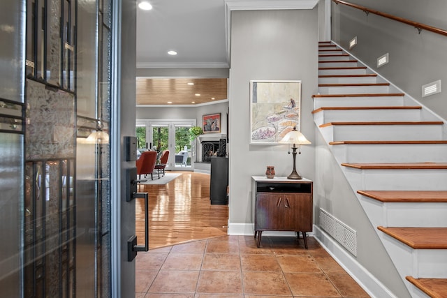 tiled foyer featuring visible vents, a fireplace with raised hearth, stairs, ornamental molding, and recessed lighting