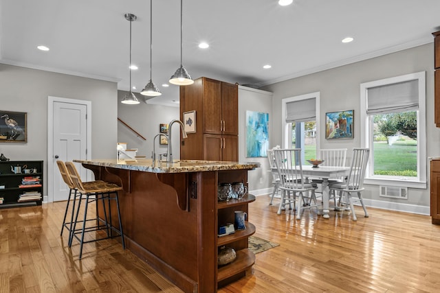 kitchen featuring light stone counters, hanging light fixtures, light hardwood / wood-style floors, and an island with sink