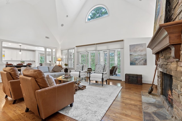 1191 Linger Longer Dr, Greensboro, GA 30642 - living room featuring a stone fireplace, light wood-style flooring, high vaulted ceiling, healthy amount of natural light, and ornate columns
