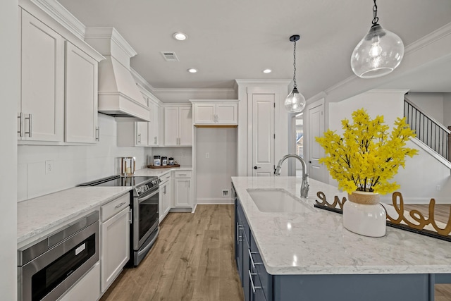 kitchen featuring visible vents, an island with sink, appliances with stainless steel finishes, premium range hood, and a sink