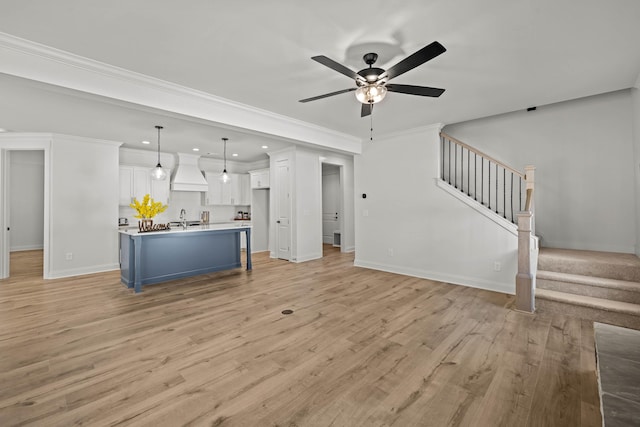 unfurnished living room with crown molding, stairway, a ceiling fan, light wood-type flooring, and baseboards