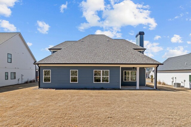 rear view of house with cooling unit, roof with shingles, a yard, and a patio