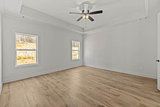 empty room with wood finished floors, visible vents, baseboards, a tray ceiling, and crown molding