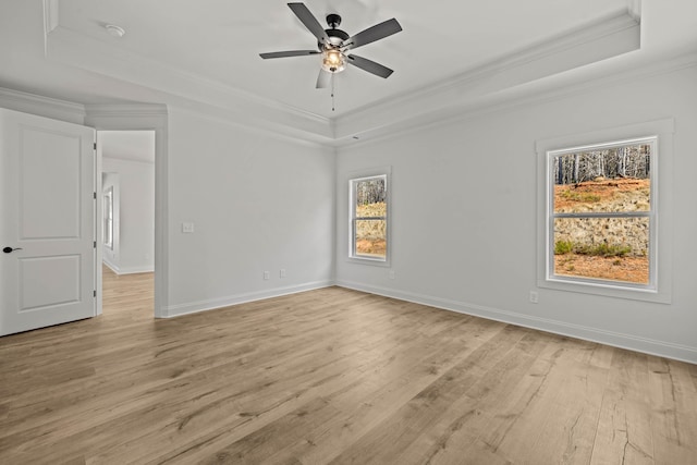 empty room with light wood finished floors, a raised ceiling, and crown molding