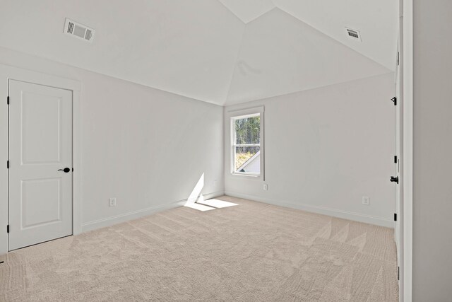 carpeted spare room featuring baseboards, visible vents, and vaulted ceiling