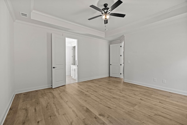 unfurnished bedroom with light wood-type flooring, a tray ceiling, visible vents, and ornamental molding