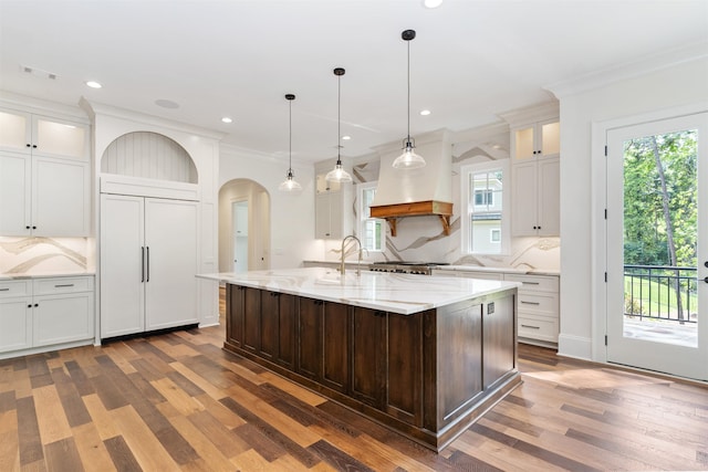 kitchen with crown molding, decorative light fixtures, paneled refrigerator, an island with sink, and white cabinets