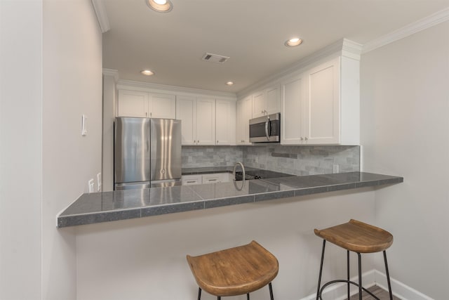 kitchen featuring a breakfast bar area, appliances with stainless steel finishes, white cabinets, decorative backsplash, and kitchen peninsula