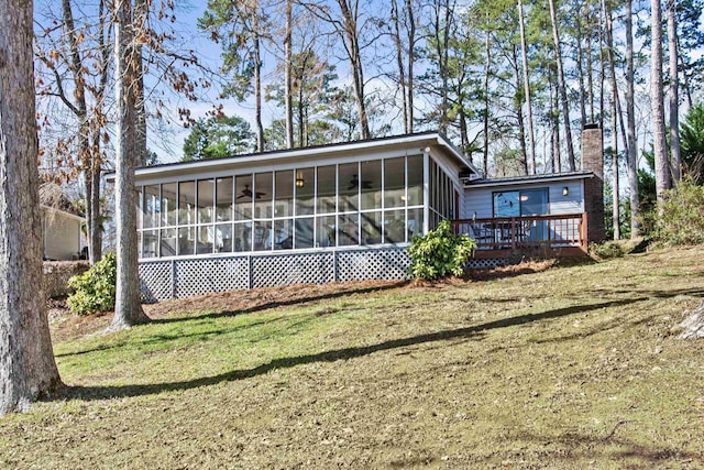 rear view of house featuring a lawn, a deck, and a sunroom