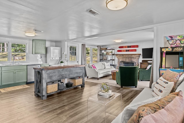 living room featuring stacked washer / dryer, wood-type flooring, sink, a fireplace, and ornamental molding