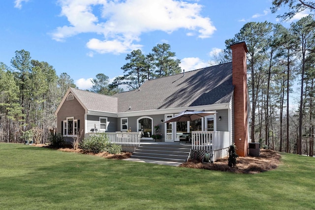 rear view of property with a shingled roof, a chimney, central AC unit, and a lawn