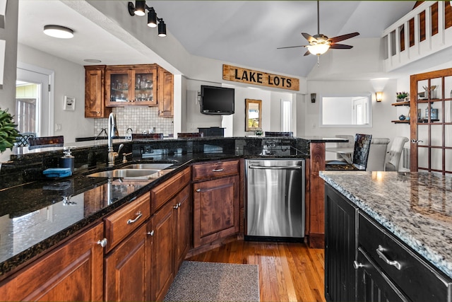 kitchen with brown cabinetry, light wood-style floors, glass insert cabinets, a sink, and dark stone counters