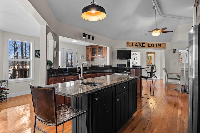 kitchen with a breakfast bar area, hanging light fixtures, a sink, dark stone countertops, and an island with sink