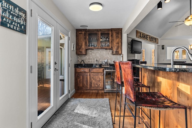 kitchen with wine cooler, a sink, wood finished floors, backsplash, and glass insert cabinets