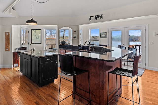 kitchen featuring dark stone counters, an island with sink, a breakfast bar, pendant lighting, and a sink