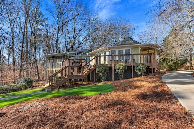 view of front of house with stairs, a front lawn, a wooden deck, and a sunroom