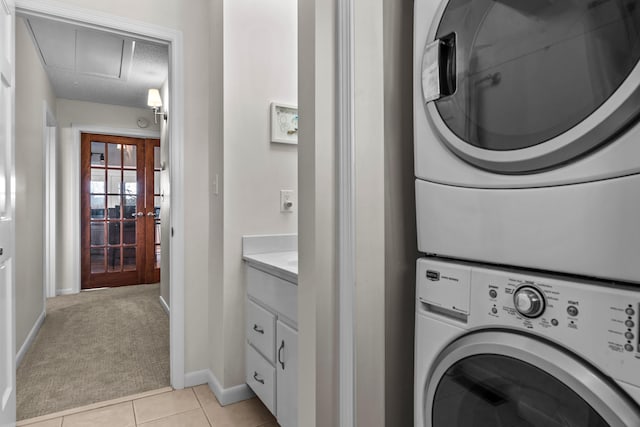 washroom featuring light tile patterned flooring, light colored carpet, laundry area, stacked washer / drying machine, and attic access