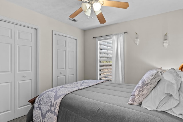 bedroom with visible vents, ceiling fan, and two closets