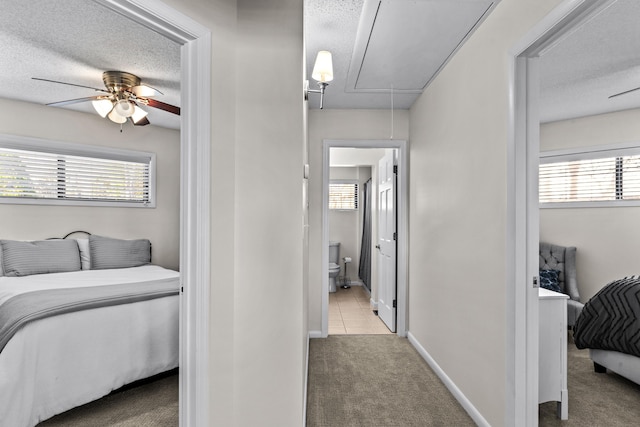 bedroom featuring light carpet, attic access, baseboards, ensuite bathroom, and a textured ceiling