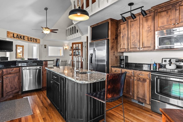 kitchen with wood finished floors, a sink, appliances with stainless steel finishes, a center island, and dark stone countertops