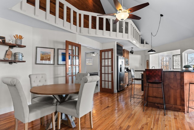 dining area with light wood finished floors, ceiling fan, high vaulted ceiling, and baseboards