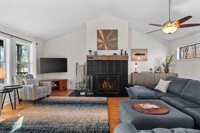 living area featuring lofted ceiling, a tiled fireplace, wood finished floors, and baseboards