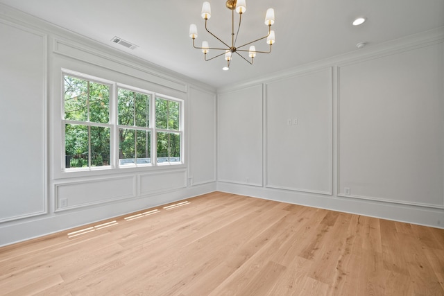 spare room featuring light wood-style floors, visible vents, a decorative wall, and a notable chandelier