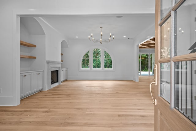 unfurnished living room featuring baseboards, an inviting chandelier, crown molding, light wood-style floors, and a fireplace