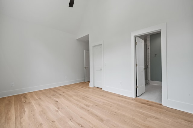 unfurnished bedroom featuring light wood-style flooring, a high ceiling, baseboards, and ensuite bathroom