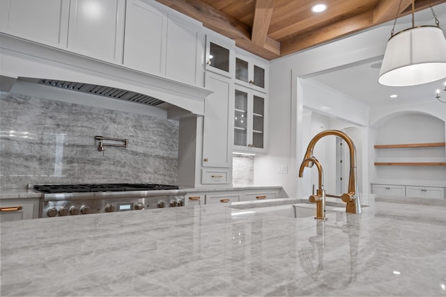 kitchen with range, glass insert cabinets, light stone countertops, premium range hood, and a sink