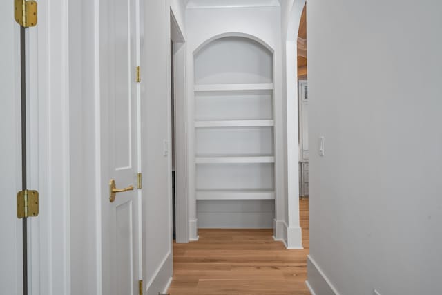 corridor featuring baseboards, light wood-type flooring, and built in features