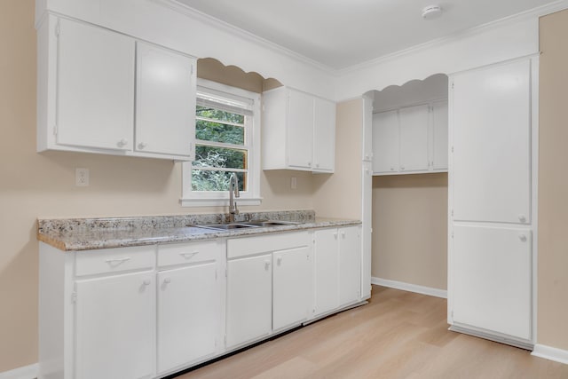 kitchen with white cabinetry, sink, ornamental molding, and light wood-type flooring