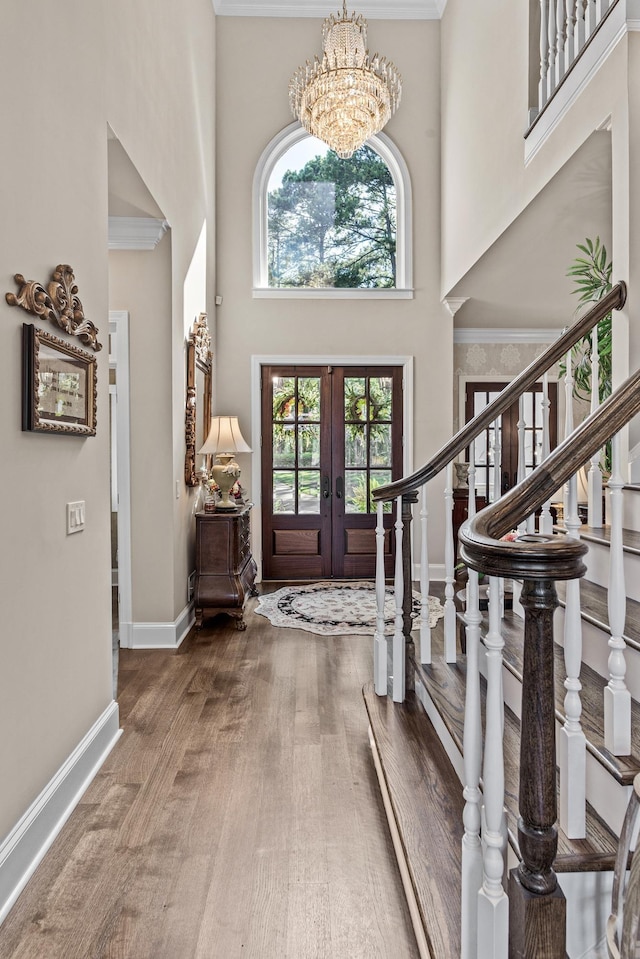 foyer with a high ceiling, wood-type flooring, an inviting chandelier, and french doors