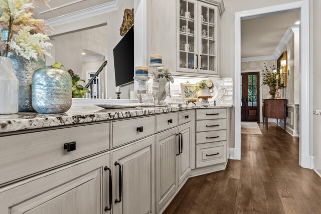 bar with light stone counters, ornamental molding, and dark hardwood / wood-style floors