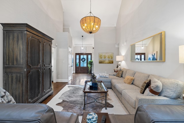 living room featuring baseboards, a notable chandelier, a high ceiling, and dark wood-type flooring