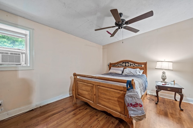 bedroom with baseboards, a ceiling fan, wood finished floors, and cooling unit