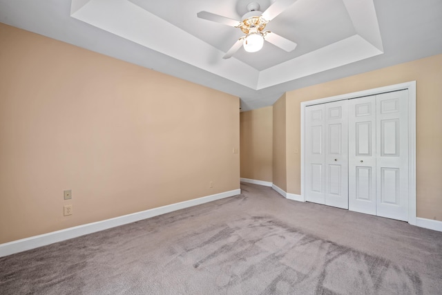 unfurnished bedroom featuring ceiling fan, a closet, a raised ceiling, and carpet