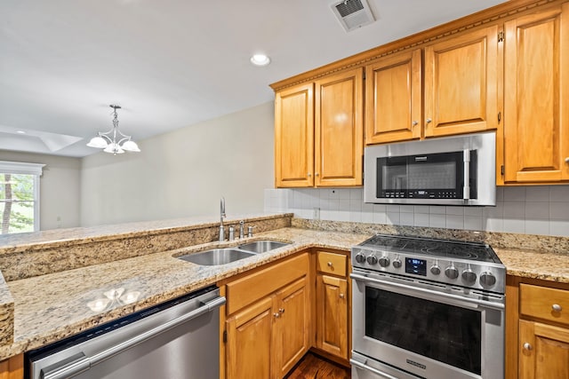 kitchen featuring appliances with stainless steel finishes, sink, backsplash, hanging light fixtures, and light stone counters